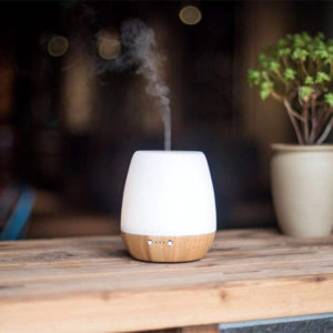 a wood base glass aroma diffuser is running with mist upward