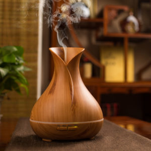 a vase shape electric diffuser in light wood color is running with mist upward