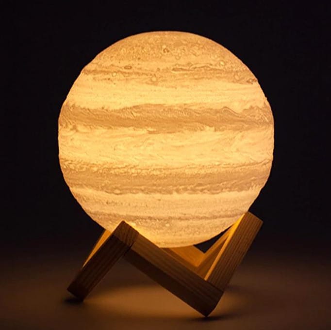 a 3d jupiter light with wood stand is glowing in the darkness